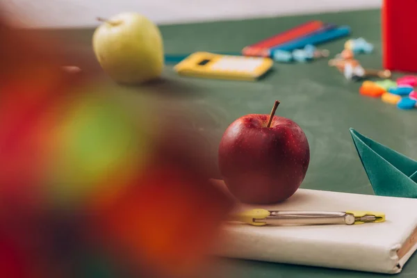 Selective focus of apple and compass divider on book near school supplies on green chalkboard — Stock Photo