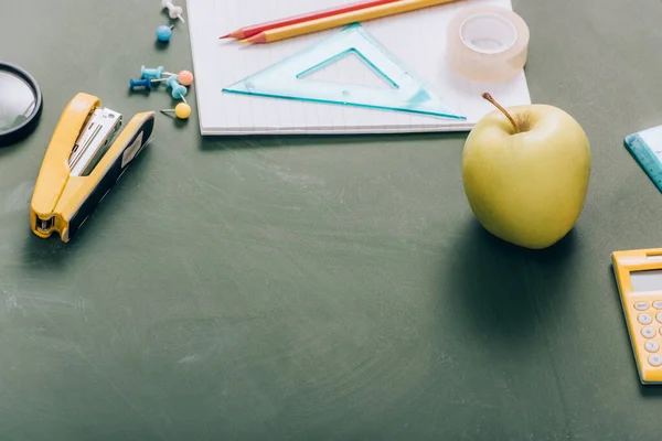 Mela matura, quaderno e materiale scolastico su lavagna verde — Foto stock