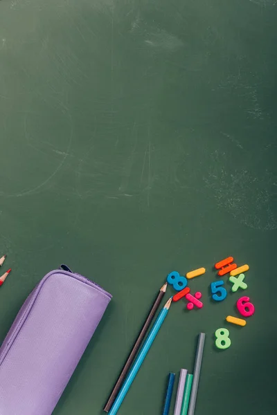 Top view of pencil case, color pencils and magnets on green chalkboard — Stock Photo