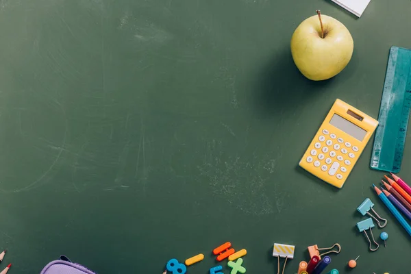 Top view of ripe apple and calculator near school supplies on green chalkboard — Stock Photo