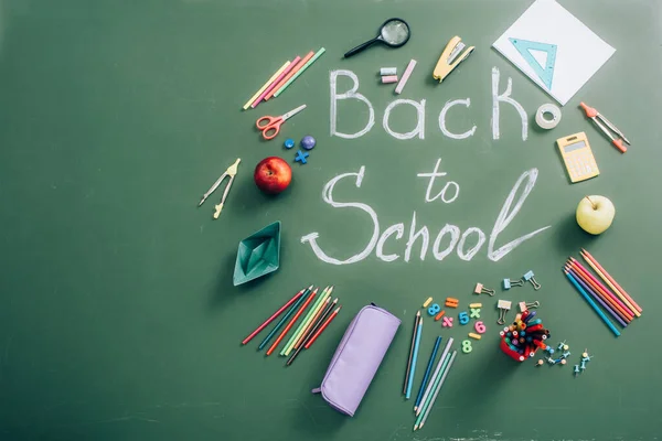 Top view of school supplies and whole apples near back to school lettering on green chalkboard — Stock Photo