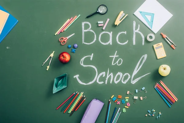 Top view of school supplies and fresh apples near back to school inscription on green chalkboard — Stock Photo