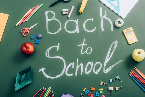 Vista superior de volta à inscrição da escola perto de artigos de papelaria da escola e maçãs inteiras em quadro-negro verde — Fotografia de Stock