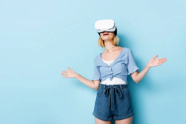 Young surprised woman in virtual reality headset gesturing on blue — Stock Photo