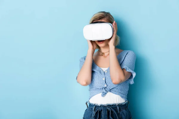 Mujer joven tocando auriculares de realidad virtual en azul - foto de stock