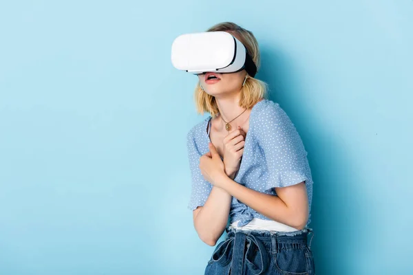 Jeune femme effrayée en réalité virtuelle casque sur bleu — Photo de stock