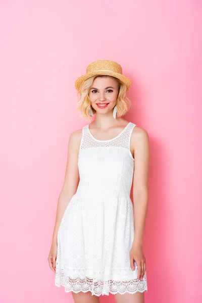 Жінка в білій сукні і солом'яному капелюсі, що стоїть на рожевому — стокове фото