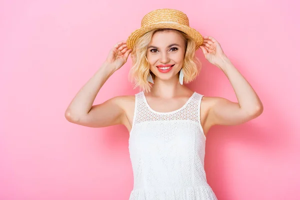 Giovane donna in abito bianco toccante cappello di paglia su rosa — Foto stock