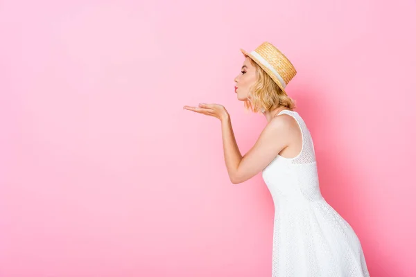 Side view of woman straw hat and dress sending air kiss on pink — Stock Photo