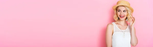 Horizontale Ernte von Frau mit Strohhut berührt Haare und schaut weg auf rosa — Stockfoto