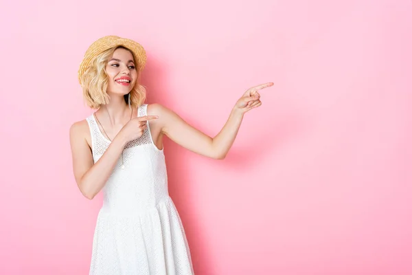 Donna in abito bianco e cappello di paglia punta con le dita sul rosa — Foto stock