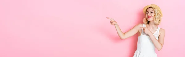 Horizontal image of woman in white dress and straw hat pointing with fingers on pink — Stock Photo