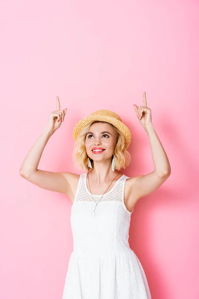 Femme en chapeau de paille pointant avec les doigts et regardant vers le haut sur rose — Photo de stock