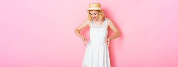 Encabezado del sitio web de la mujer en sombrero de paja que apunta con los dedos y mirando hacia abajo en rosa - foto de stock