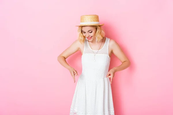 Woman in straw hat pointing with fingers and looking down on pink — Stock Photo