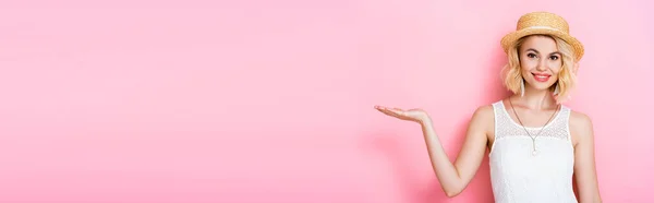 Horizontal crop of woman in straw hat pointing with hand on pink — Stock Photo