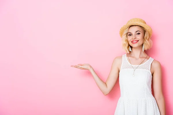 Mujer en sombrero de paja señalando con la mano en rosa - foto de stock