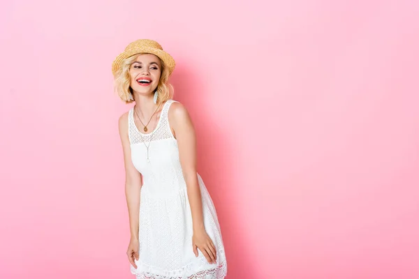 Збуджена жінка в солом'яному капелюсі сміється і дивиться на рожевий — стокове фото
