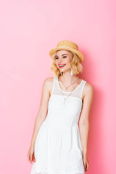 Woman in straw hat and dress standing and looking away on pink — Stock Photo