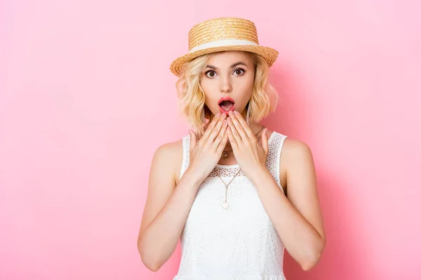 Shocked young woman in straw hat covering mouth on pink — Stock Photo