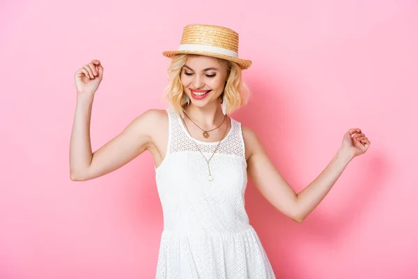 Young woman in straw hat and dress looking down while dancing on pink — Stock Photo