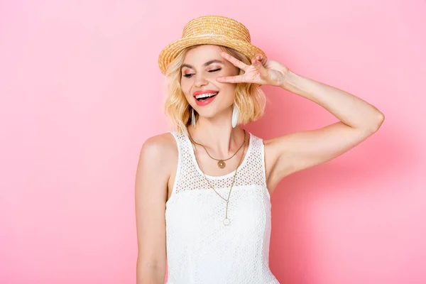 Young woman in straw hat showing peace sign on pink — Stock Photo