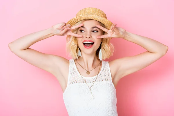 Young woman in straw hat showing peace sign on pink — Stock Photo
