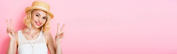 Cosecha panorámica de la mujer en sombrero de paja que muestra signo de paz en rosa - foto de stock