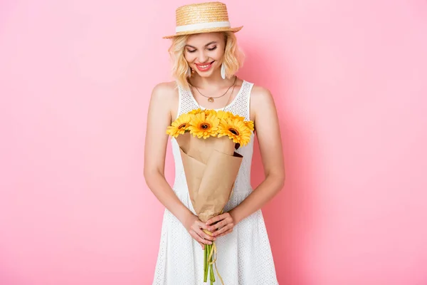Young woman in straw hat looking at flowers on pink — Stock Photo