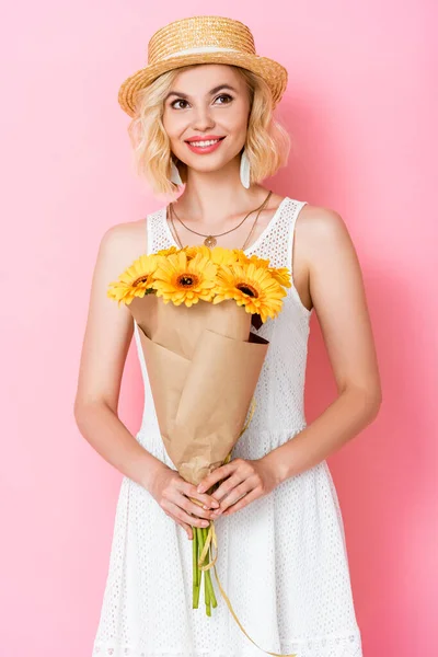 Mujer joven en sombrero de paja sosteniendo flores amarillas en rosa - foto de stock