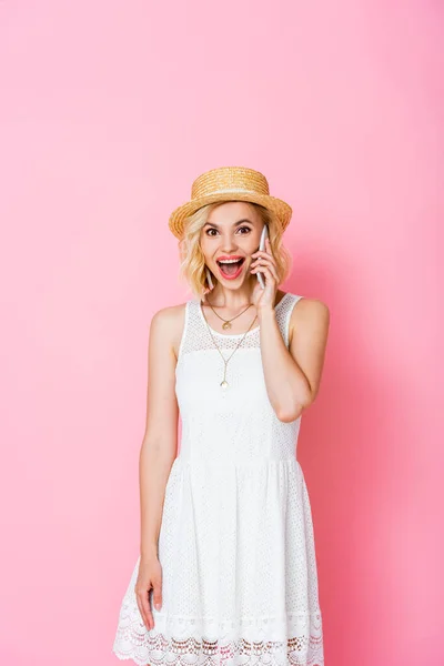 Aufgeregte Frau mit Strohhut redet auf Smartphone auf rosa — Stockfoto