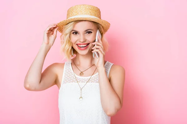 Donna toccando cappello di paglia e parlando su smartphone su rosa — Foto stock