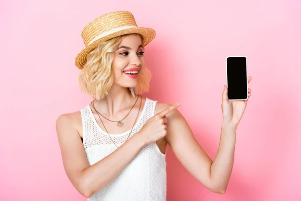 Mulher de chapéu de palha apontando com o dedo para o smartphone com tela em branco no rosa — Fotografia de Stock