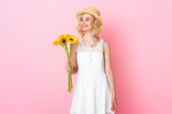 Woman in straw hat and white dress holding yellow flowers on pink — Stock Photo
