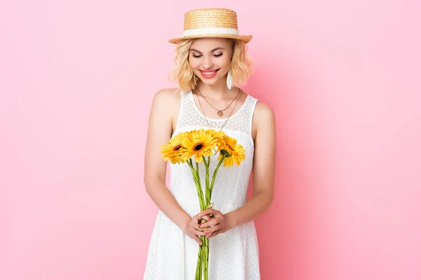Woman in straw hat and white dress looking at yellow flowers on pink — Stock Photo
