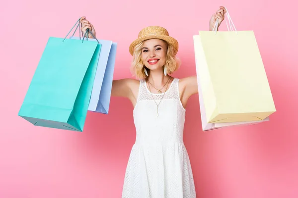 Mulher de chapéu de palha e vestido branco segurando sacos de compras em rosa — Fotografia de Stock