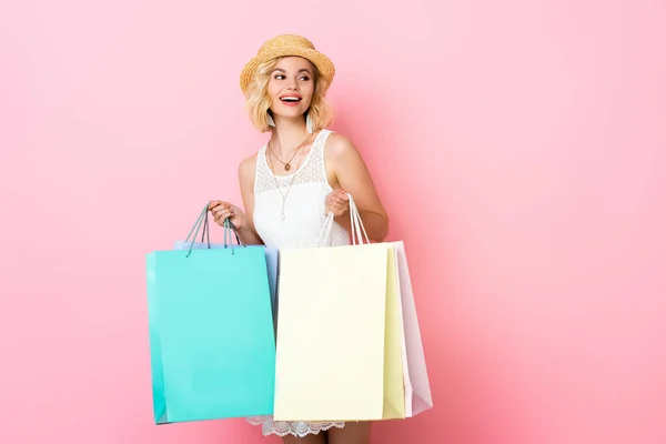 Mulher animado em chapéu de palha e vestido branco segurando sacos de compras em rosa — Fotografia de Stock