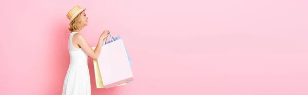 Panoramic concept of young woman in white dress holding shopping bags on pink — Stock Photo