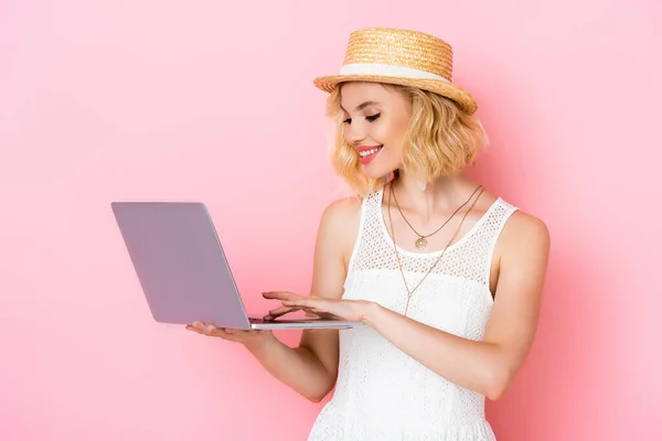 Jeune femme en chapeau de paille en utilisant un ordinateur portable sur rose — Photo de stock