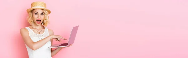 Horizontal crop of excited woman in straw hat pointing with finger at laptop on pink — Stock Photo