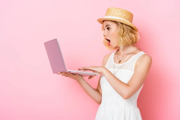 Mulher chocada em chapéu de palha olhando para laptop em rosa — Fotografia de Stock