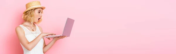Panoramic orientation of shocked woman in straw hat looking at laptop on pink — Stock Photo