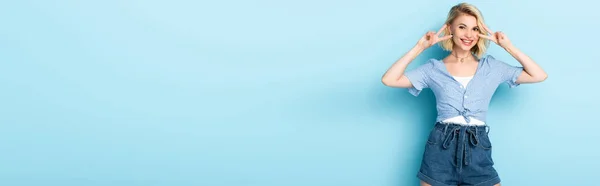 Panoramic crop of woman in shorts showing peace sign on blue — Stock Photo