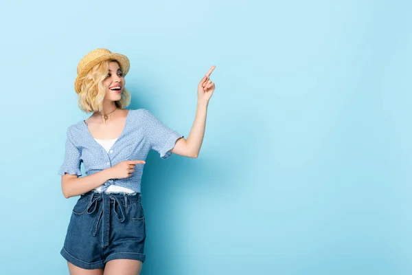 Femme en chapeau de paille pointant avec les doigts et regardant loin sur bleu — Photo de stock