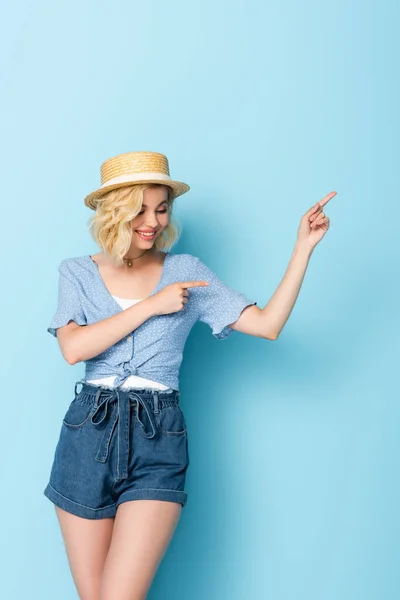 Frau mit Strohhut zeigt mit den Fingern und schaut weg auf blau — Stockfoto