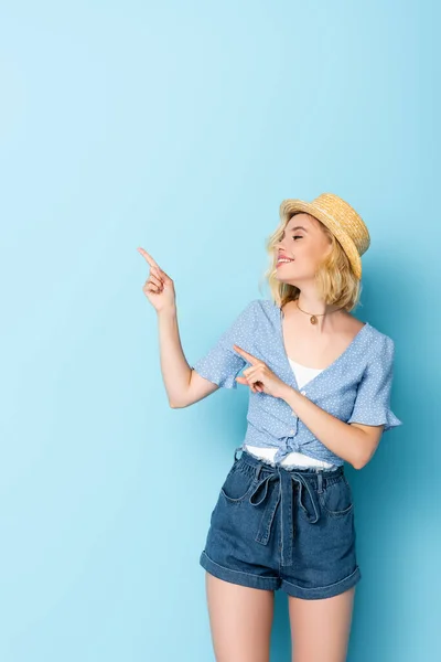 Femme en chapeau de paille pointant avec les doigts et regardant loin sur bleu — Photo de stock