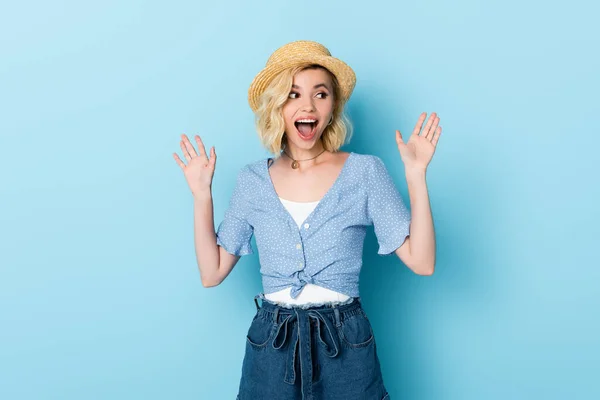 Возбужденная молодая женщина в соломенной шляпе жестом на синий — стоковое фото