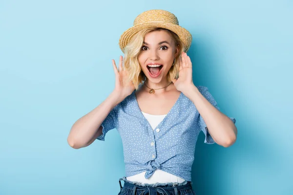 Animado jovem mulher no chapéu de palha gesticulando e olhando para a câmera no azul — Fotografia de Stock