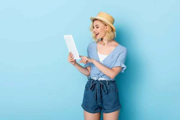 Excited woman in straw hat using digital tablet on blue — Stock Photo
