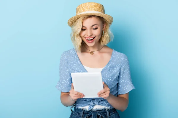 Donna in cappello di paglia guardando tablet digitale su blu — Foto stock